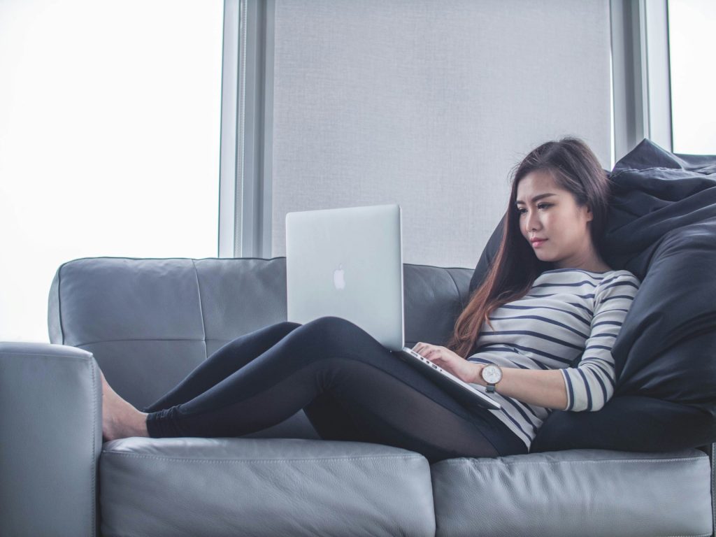 Woman reclining on couch, working on laptop.