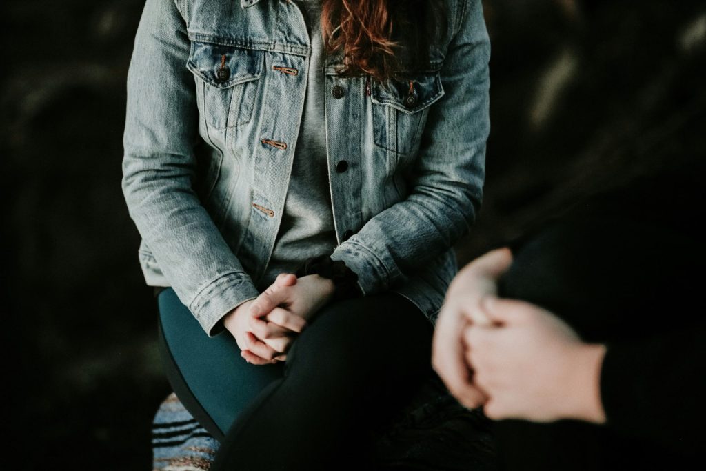 Person in denim jacket with hands clasped.