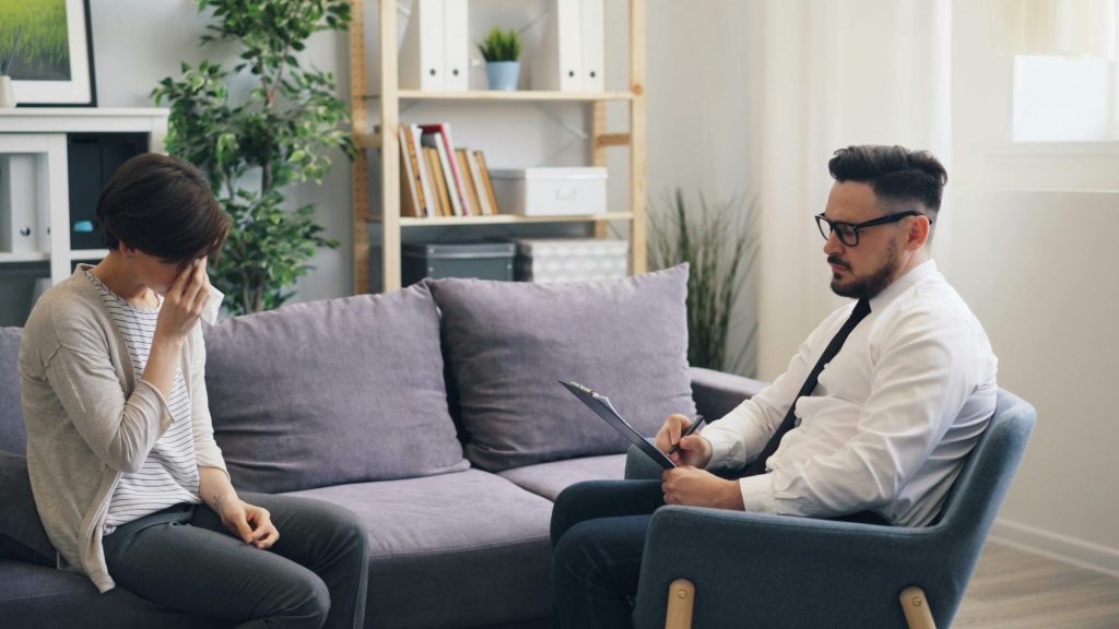 Therapist taking notes while woman looks distressed.