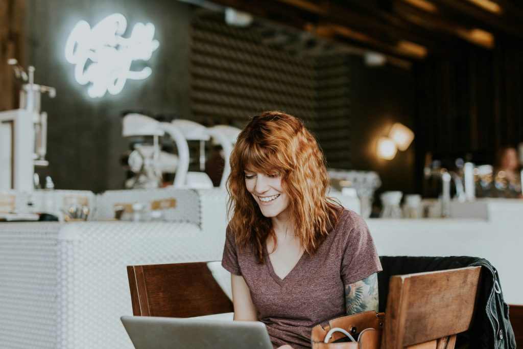 Smiling woman working on laptop in cafe.